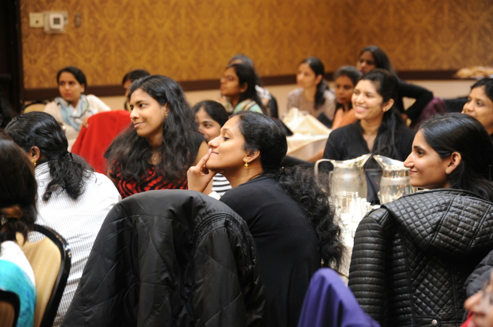 Women seated at round tables in a meeting room, listening to a speaker out of frame