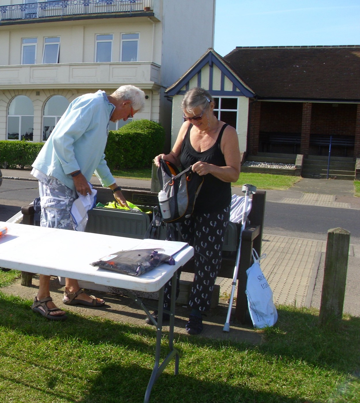 Two people setting up a folding table on a patch of grass before an outdoor event