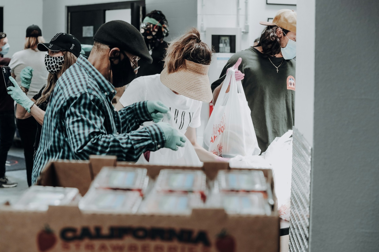 Volunteers in masks and gloves packing bags of food behind a table stacked with produce boxes