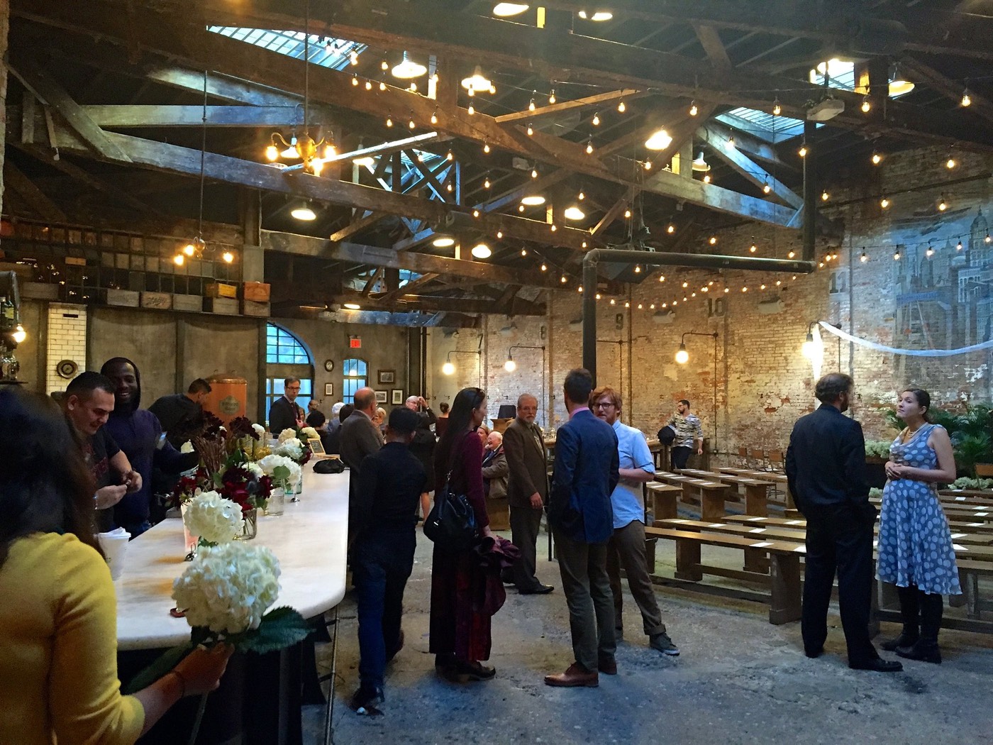 Guests arriving and greeting each other in a warm, string-lit hall with long tables